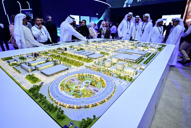 men in long white robes and scarves standing on a model of an industrial park
